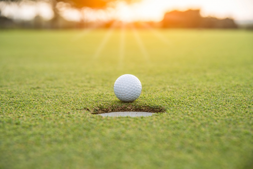 Golfer is putting golf ball on green grass at golf course for game with blur background and sunlight ray