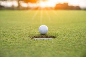Golfer is putting golf ball on green grass at golf course for game with blur background and sunlight ray